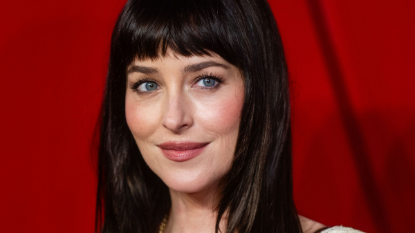 Dakota Johnson wears a sheer cream lace dress and long hair with bangs.